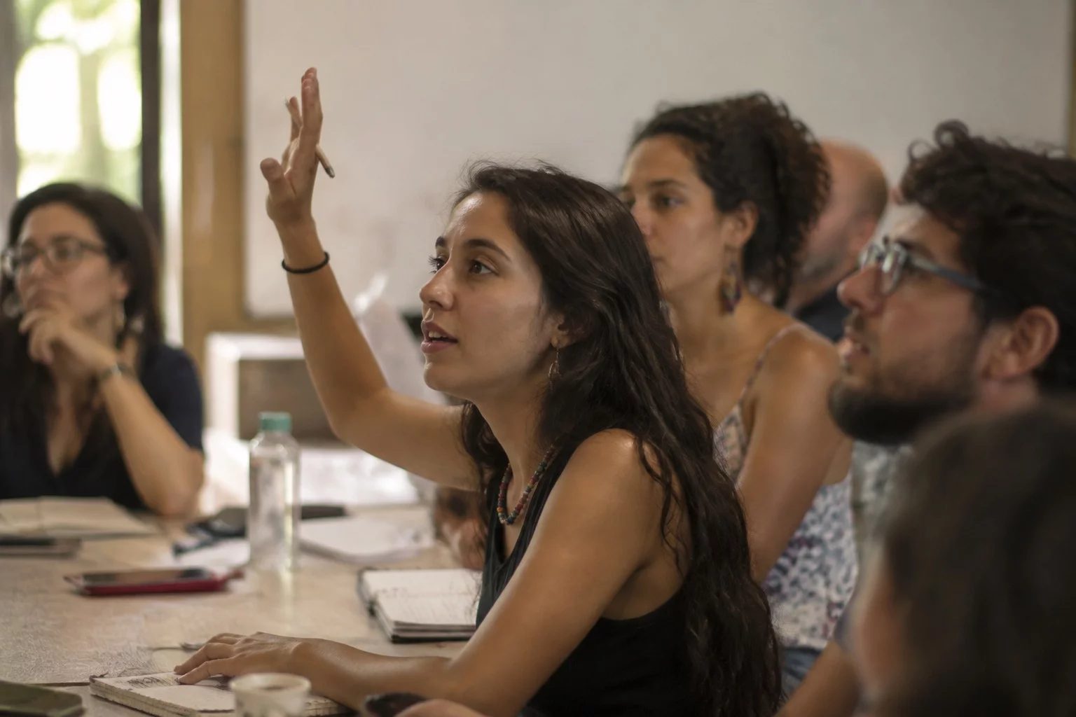 Estudante levantando a mão em uma mesa de seminário coberta de anotações