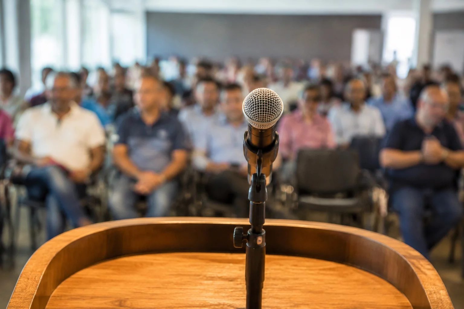 Microfone sobre uma tribuna, com a plateia sentada desfocada ao fundo